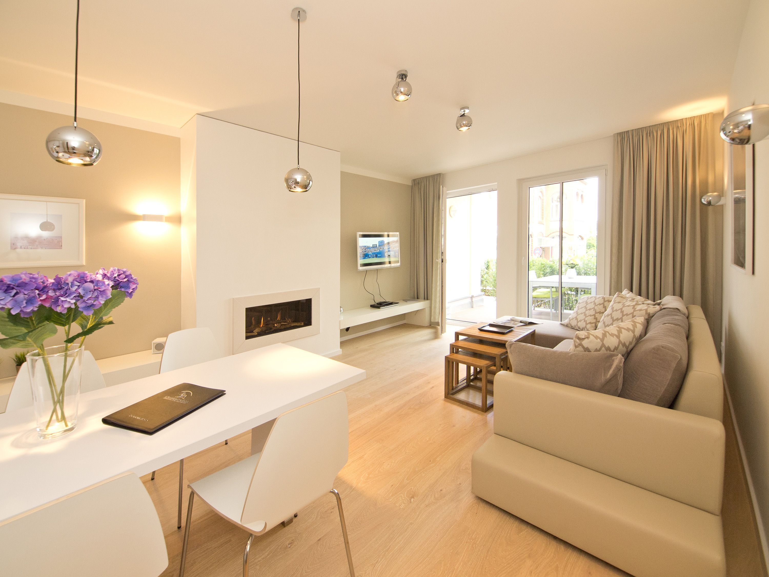 A modern living room with a sofa, a dining table with chairs, a fireplace, and a TV.