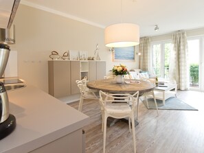A modern kitchen with a round dining table, white chairs, and a large pendant light. - Dünenpalais, App. 04 (Heringsdorf)