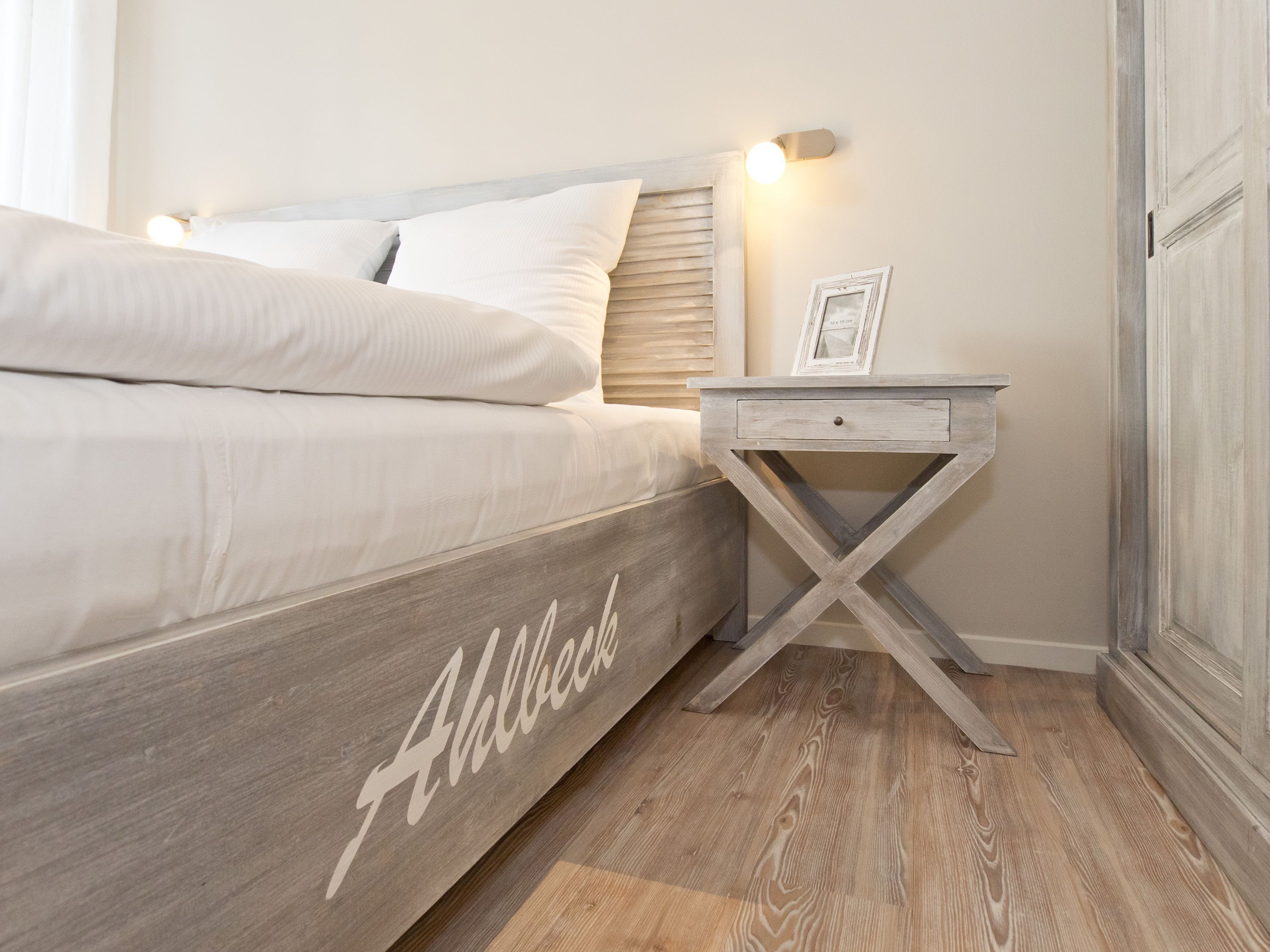 A bedroom with a bed, a nightstand with a drawer, and a wooden floor.