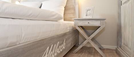 A bedroom with a bed, a nightstand with a drawer, and a wooden floor.