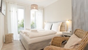 Et soveværelse med en seng, en fletstol, et natbord med lampe og et vindue med gardiner.