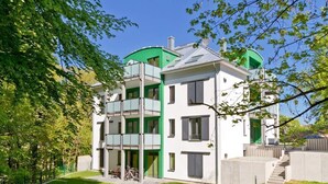 A modern multi-story residential building with a green accent on the upper floors, surrounded by a well-maintained lawn and trees. - Residenzen am Kulm, Villa Dorian 10 (Heringsdorf)