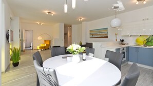 A modern kitchen with white cabinets, a yellow fruit bowl, and a dining area with a round table and chairs. - Residenzen am Kulm, Villa Dorian 10 (Heringsdorf)