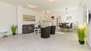 A modern living room with a grey sofa, black ottomans, and a dining area with a white table and chairs. - Residenzen am Kulm, Villa Dorian 10 (Heringsdorf)