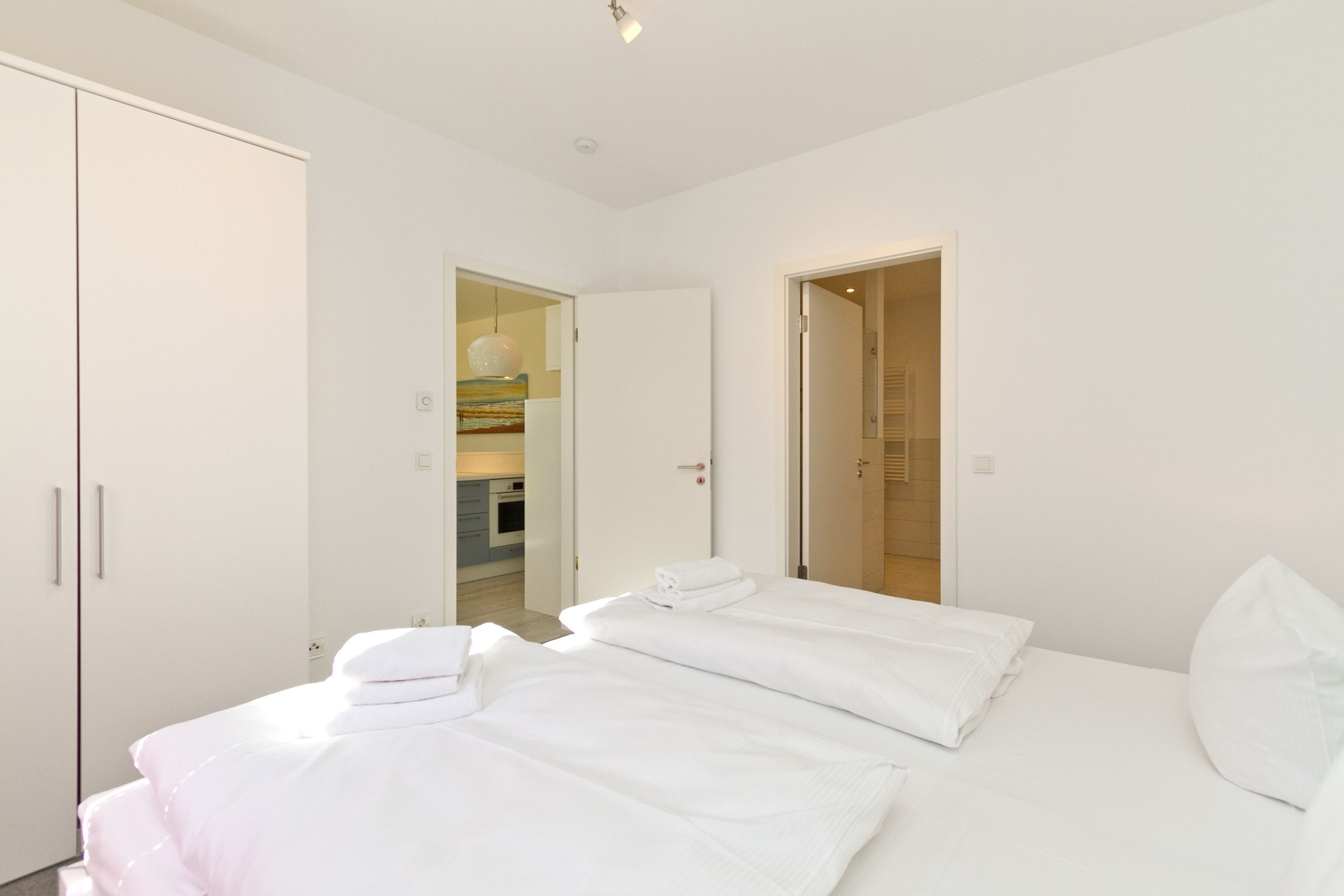 A modern hotel room with a large bed, a wardrobe, and a bathroom visible through an open door.