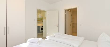 A modern hotel room with a large bed, a wardrobe, and a bathroom visible through an open door.