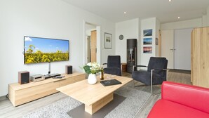 Un salon moderne avec un téléviseur à écran plat, une table basse en bois, un canapé rouge et deux fauteuils noirs.