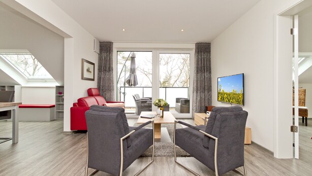 Un salon moderne avec un canapé rouge, des fauteuils gris, une table basse en bois et un téléviseur fixé au mur.