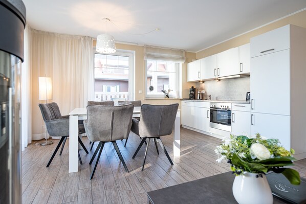 A modern kitchen with white cabinets, a dining table with chairs, and a vase with flowers.