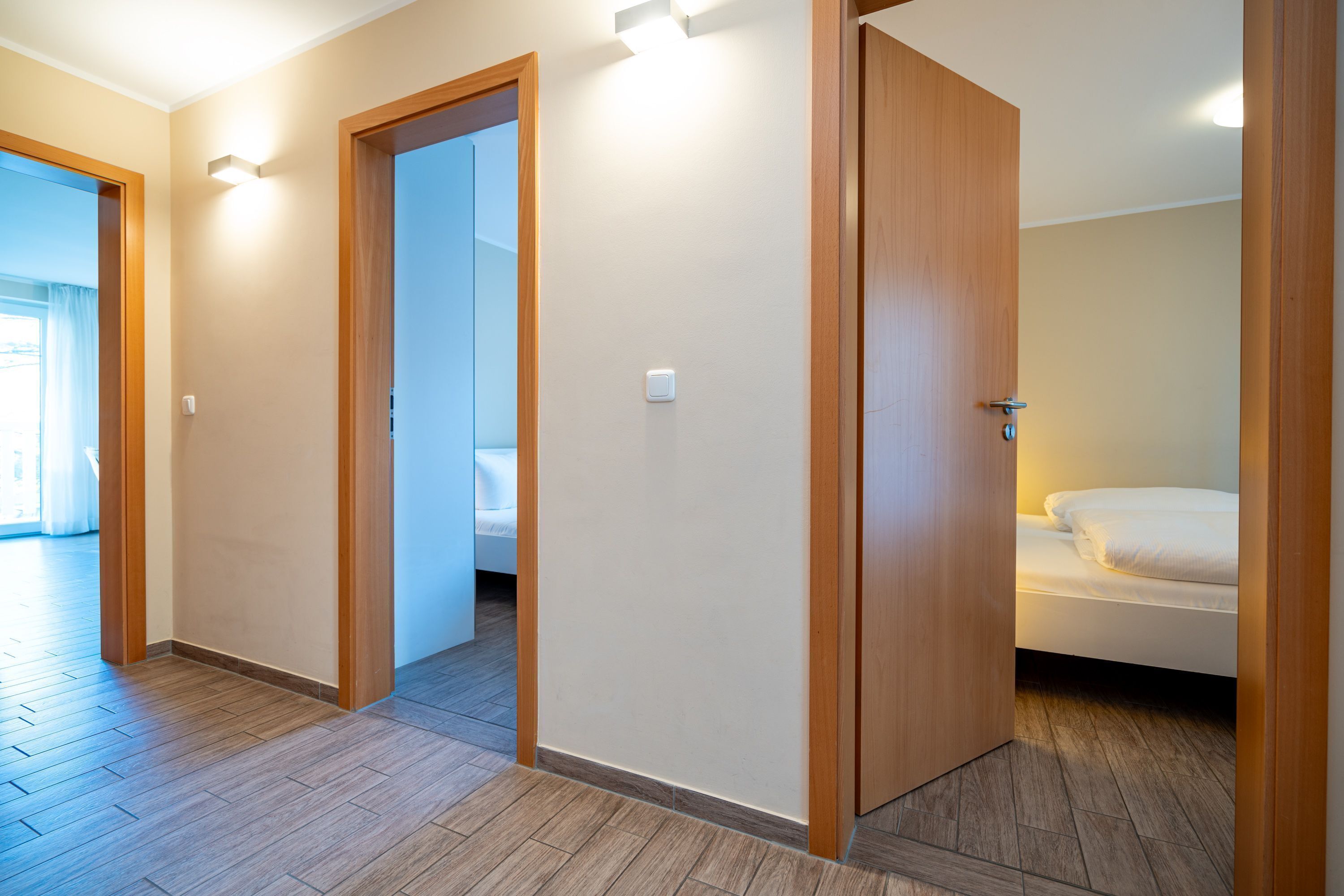Une chambre d’hôtel avec un plancher en bois, un lit avec une literie blanche et une porte donnant sur une autre pièce.