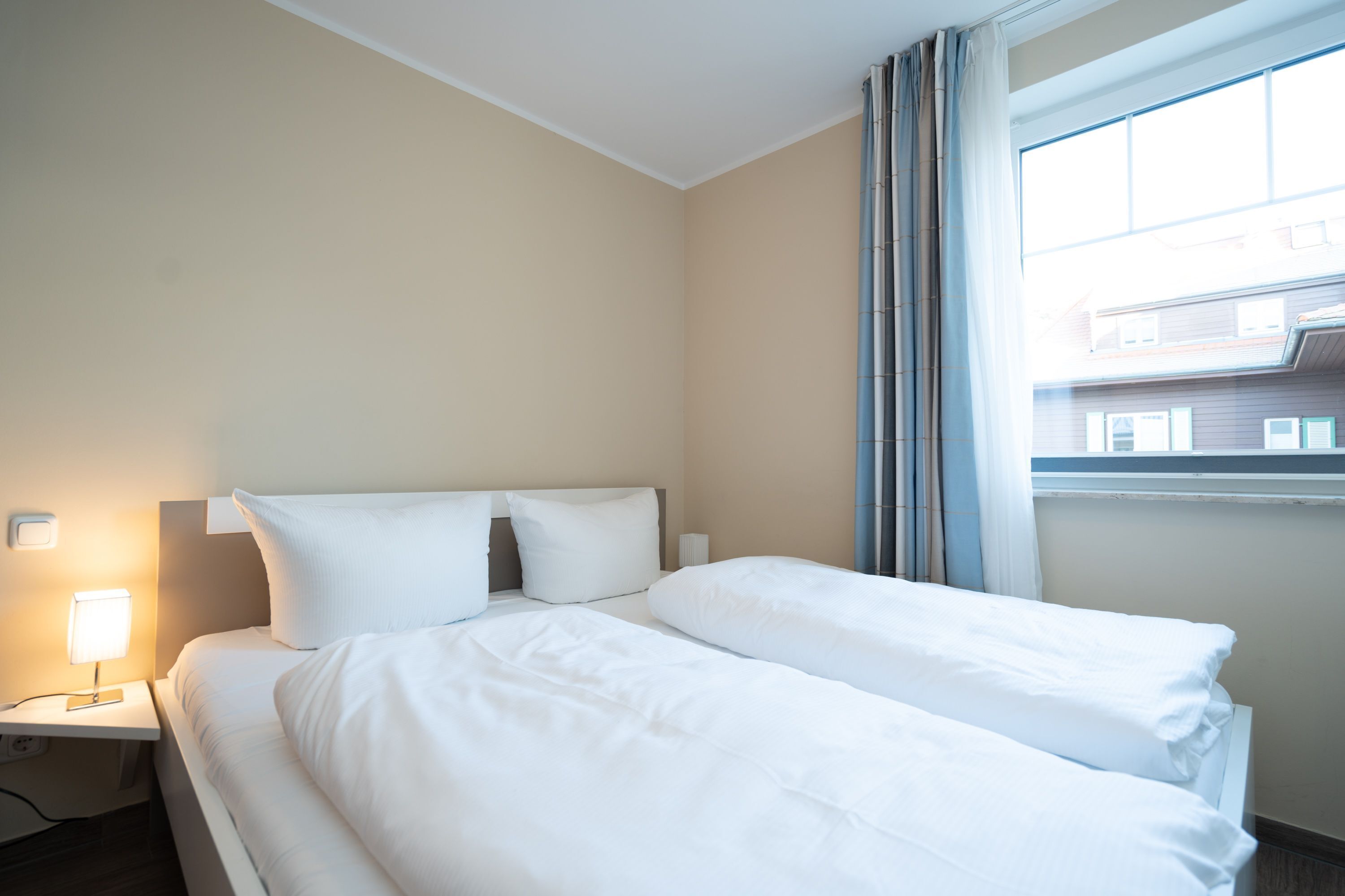 A hotel room with a bed, a nightstand with a lamp, and a window with curtains.