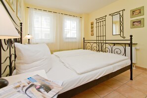 Een net opgemaakt bed in een kamer met een raam, een lamp en een spiegel aan de muur.