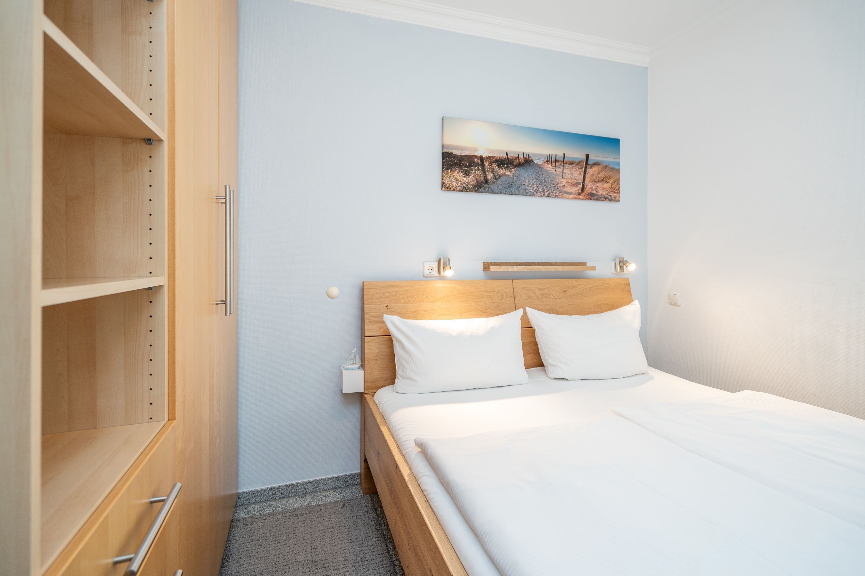 Una camera da letto con un letto di legno, biancheria bianca, un comodino e un quadro appeso al muro.