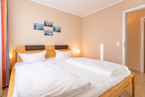A neatly made bed with white linens, a wooden headboard, and two bedside lamps.