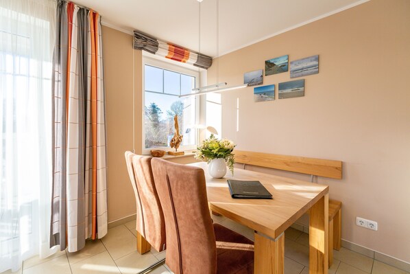 Une chambre moderne avec un bureau en bois, une chaise rembourrée, un vase de fleurs et une fenêtre donnant sur des arbres.