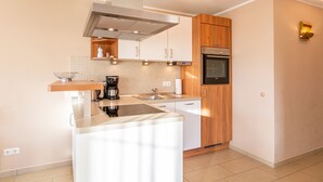 A modern kitchen with white cabinets, a stainless steel range hood, a built-in oven, and a countertop with a coffee maker.