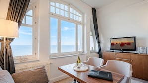 Et værelse med havudsigt, et spisebord med en flaske og glas, et fjernsyn på et træskab og en sofa.