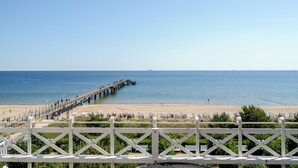A beach with a pier extending into the water, a sandy beach area, and a white fence in the foreground.