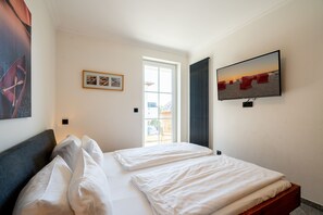Ein Hotelzimmer mit einem Bett, einem an der Wand montierten Fernseher und einem Fenster mit Vorhängen.