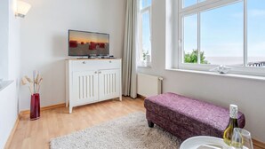 Habitació moderna amb televisió, un armari blanc, una banca i una finestra gran.