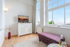 A modern room with a TV, white cabinet, bench, and large window. - Villa Dora, App. 08, Germany (Heringsdorf)
