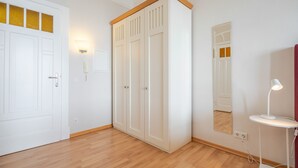 Habitació amb terra de fusta, armari blanc, mirall i una taula petita amb una làmpada.