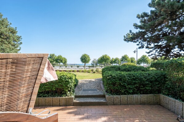 A patio area with a wicker chair, a stone pathway leading to a grassy area, and a view of a body of water.