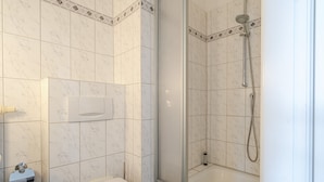 A bathroom with a toilet, a shower with a glass door, and a marble-tiled wall.