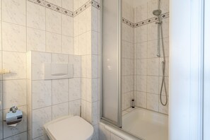 A bathroom with a toilet, a shower with a glass door, and a marble-tiled wall.