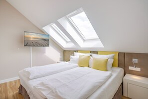 A bedroom with a bed, a nightstand, a lamp, and a painting of a beach scene. - Dünenpalais, App. 22 (Heringsdorf)