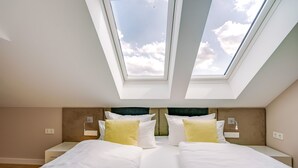 Un dormitorio con tragaluz, una cama con ropa de cama blanca y una mesita de noche con lámpara.