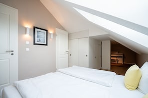 Une chambre avec un plafond en pente, un lit avec une literie blanche, un oreiller jaune et un tableau encadré au mur.