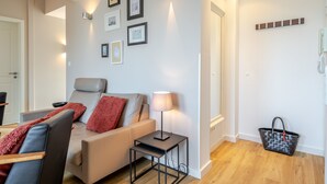 Una sala de estar moderna con un sofá, sillones, una mesita y una lámpara. Hay cuadros enmarcados en la pared y un teléfono también en la pared.