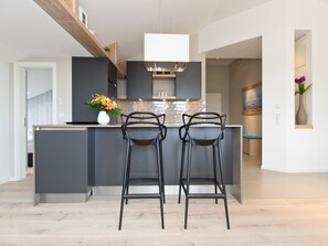 A modern kitchen with a central island, two bar stools, and a vase of flowers. - Dünenpalais, App. 25 (Heringsdorf)