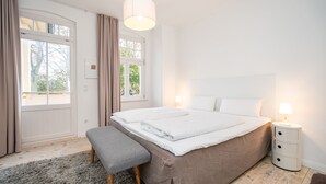Et soveværelse med en stor seng, en bænk, et natbord med lampe og et vindue med gardiner.