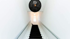En trappe med hvide gelændere og en sort, rund lampe med struktur over sig.