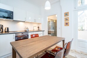 Une cuisine moderne avec des meubles blancs, des appareils en acier inoxydable et une table à manger en bois, accompagnée de chaises.