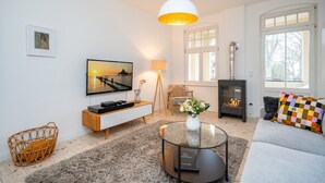 En moderne stue med et fladskærms-tv, et glasbord, en sofa, en pejs og et stort vindue.