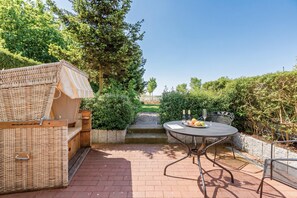 Eine Terrasse mit einer Rattan-Couch, einem runden Metalltisch mit Stühlen und einer kleinen Treppe, die zu einer Rasenfläche führt.