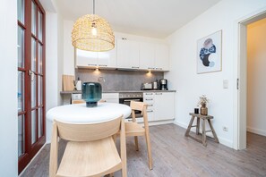 Uma cozinha moderna com armários brancos, uma mesa de jantar redonda e um lustre pendente.