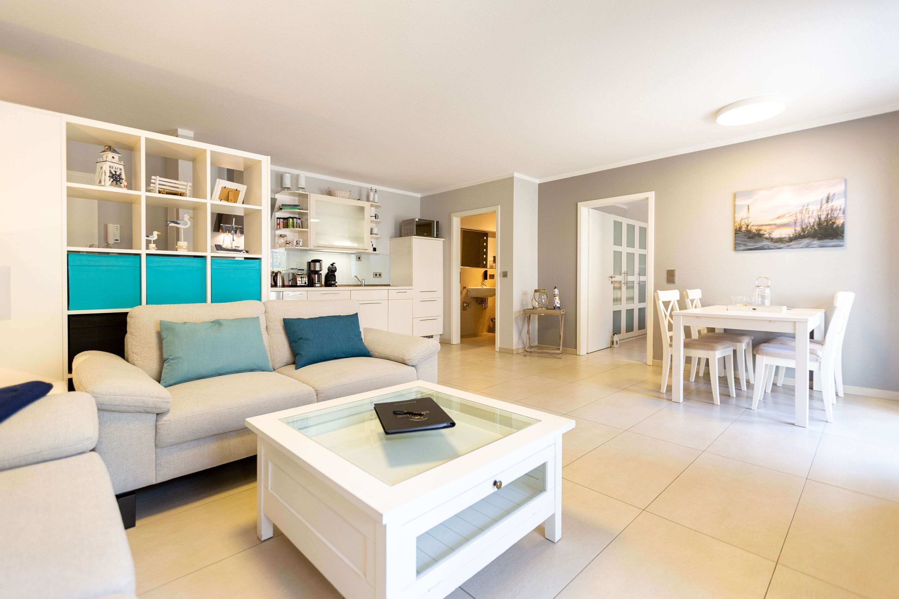 Una sala moderna con un sofá, una mesa de centro y un comedor con una mesa y sillas. Hay una cocina con armarios y electrodomésticos.