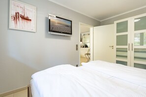 A bedroom with a bed, a television mounted on the wall, and a wardrobe with frosted glass doors. - Domizil am Hang, App. B09 (Heringsdorf)
