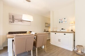 A modern kitchen with a dining area, featuring a white cabinet, a hanging light, and a wall-mounted picture. - Domizil am Hang, App. B08 (Heringsdorf)