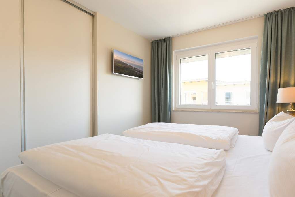 Ein Hotelzimmer mit zwei Betten, einem Fenster mit Vorhängen, einem Gemälde an der Wand und einer Lampe auf dem Nachttisch.