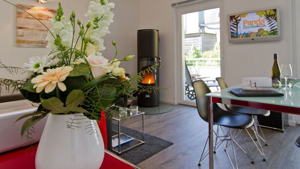 Una sala de estar moderna con una mesa de comedor de cristal, una chimenea y un jarrón con flores.