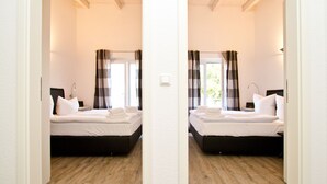 Reflejo de un dormitorio con dos camas, suelo de madera y cortinas.