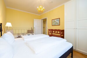 Une chambre d’hôtel avec un grand lit, une chaise en bois, une armoire blanche et un lustre.