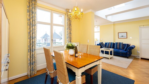 A dining area with a wooden table, chairs, and a chandelier. There is a sofa and a window with curtains in the background. - The Villa, App. 8, Germany (Heringsdorf)