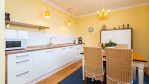 A modern kitchen with white cabinets, a microwave, and a dining area with wicker chairs and a wooden table. - The Villa, App. 8, Germany (Heringsdorf)