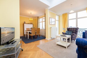 Un salon avec un téléviseur, un coin repas avec une table et des chaises, et un balcon avec vue.